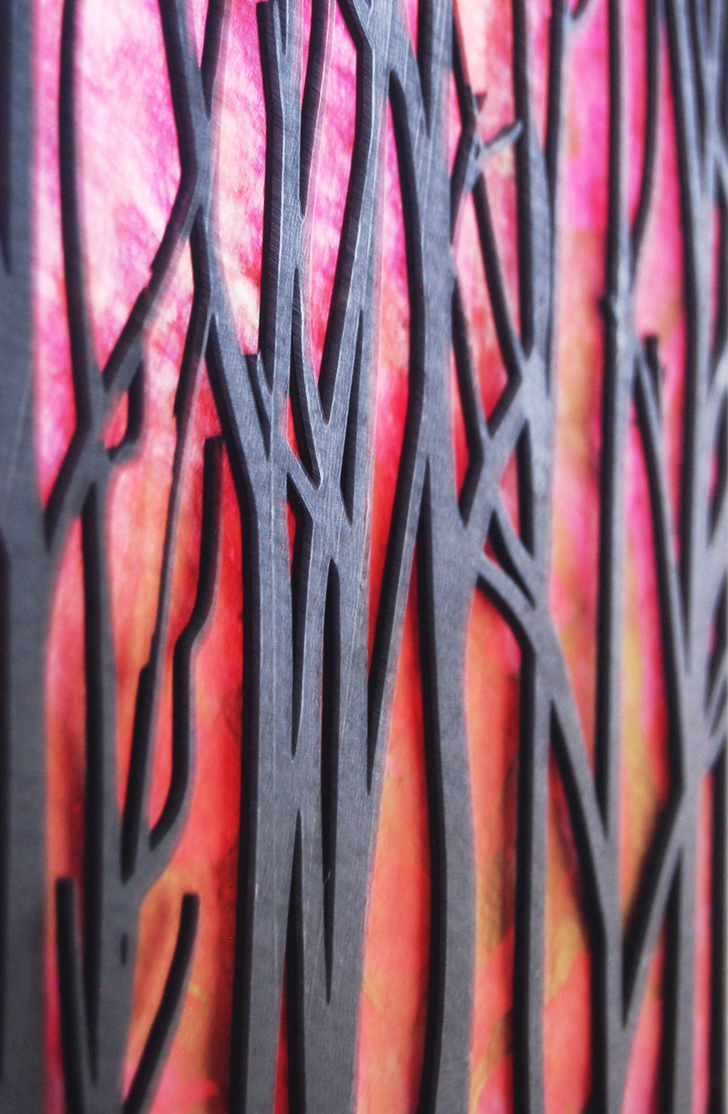 Close-up of crimson hand-painted paper panel through laser-cut tree silhouette