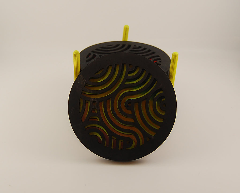 Round laser-cut coaster set with colorful layered designs and yellow holder posts