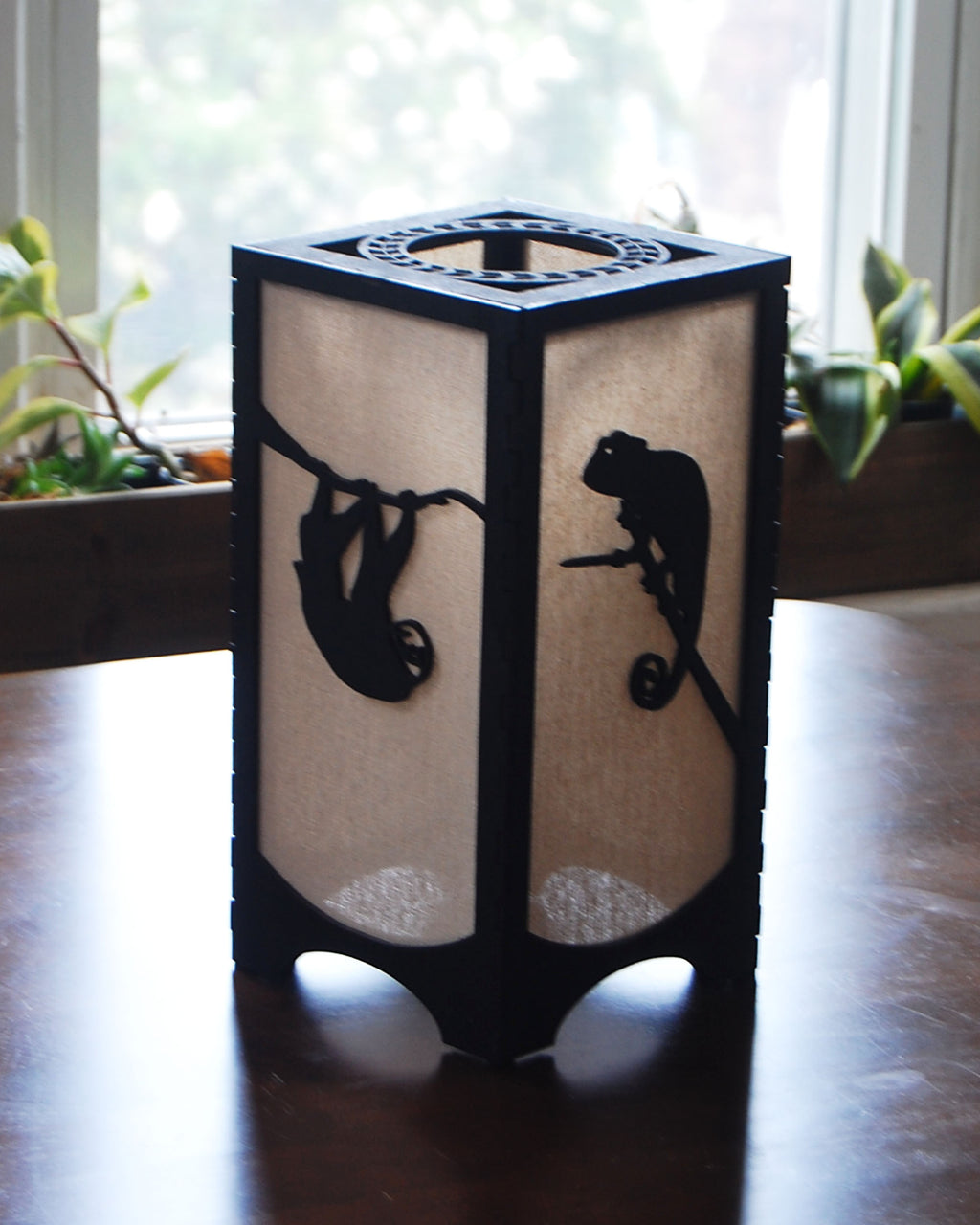Handmade laser-cut wildlife lantern — sloth and chameleon silhouettes in natural light